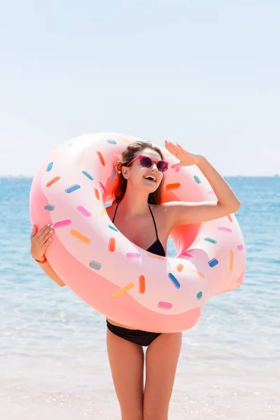 Ciesząc się opalenizny i wakacji. Portret szczęśliwej dziewczyny patrząc przez nadmuchiwane pierścień pobyt na plaży morskiej. Koncepcja wakacji letnich — Zdjęcie stockowe
