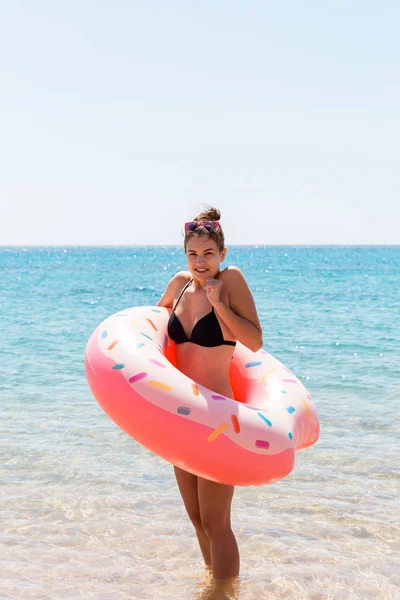 Young woman with inflatable ring cold shivering sad crossed arms black bikini swimsuit standing in sea water. Summer holidays and vacation concept