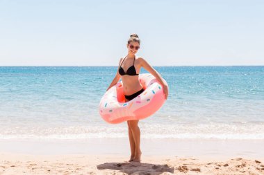 Genç seksi kadın deniz sahilinde kalıp şişme halka çöreklerle oynuyor ve eğleniyor. Yaz tatili ve tatil konsepti