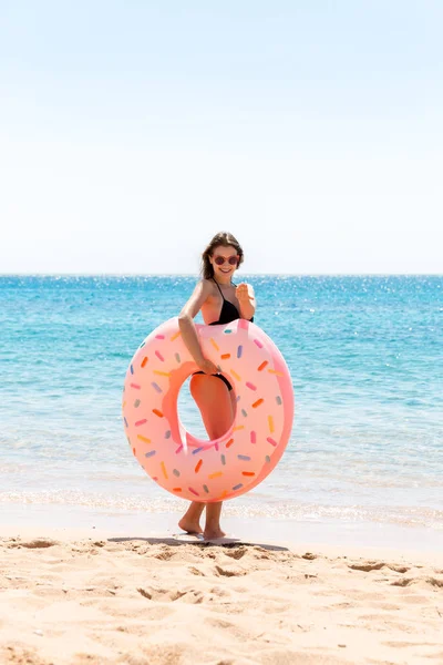Hembra feliz en la playa jugando con un anillo de rosquilla inflable. Vacaciones de verano y concepto de vacaciones —  Fotos de Stock