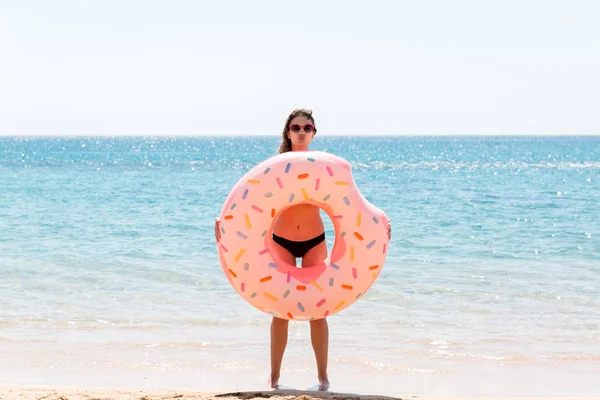 Счастливая женщина на пляже играет с надувным кольцом пончика. Летние каникулы и отдых — стоковое фото