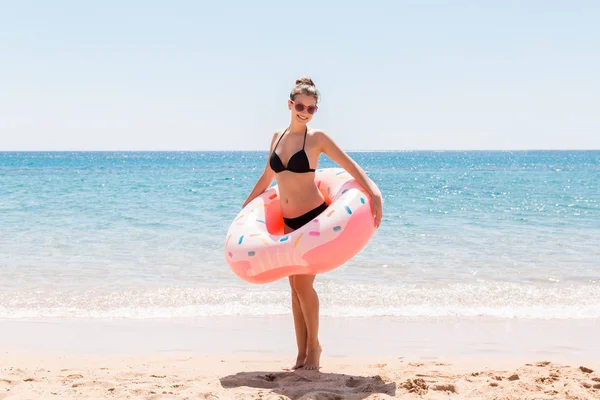 Молодая сексуальная симпатичная женщина остается на морском пляже и играет с пончиком в кольцо и получает удовольствие. Летние каникулы и отдых — стоковое фото