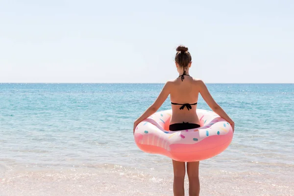 Jovem bonita ficar na praia do mar com donut anel inflável e se diverte. Conceito de férias e férias de verão — Fotografia de Stock