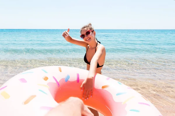Женщина зовет купаться в море и машет рукой. Девушка отдыхает на надувном кольце в море. Летние каникулы и отдых — стоковое фото
