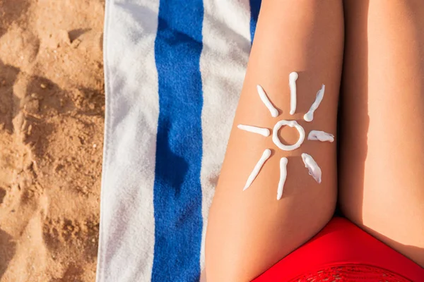 La crema solar se dibuja en forma de sol en la pierna de la mujer bronceada que se está relajando en la toalla en la playa. Concepto de cuidado del cáncer — Foto de Stock