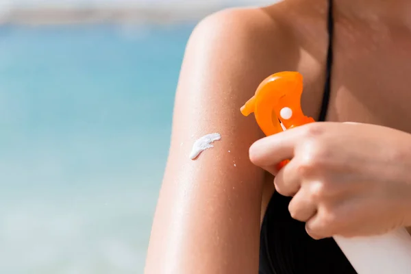 Woman is putting sun lotion on her shoulder at the sea background — Stock Photo, Image