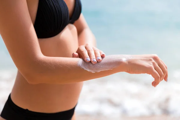 Pretty girl is putting sun lotion on her hand at the beach — Stock Photo, Image