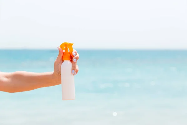 Przycięty obraz dłoni kobiety trzymającej spray z filtrem przeciwsłonecznym na tle morza — Zdjęcie stockowe