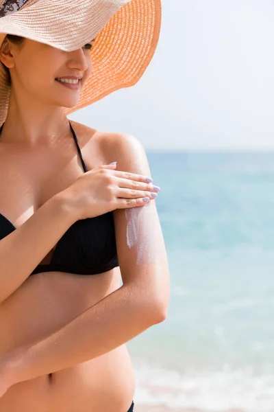 Protector solar protector solar. Mujer en un sombrero poniendo crema solar en el hombro al aire libre bajo el sol en el hermoso día de verano — Foto de Stock