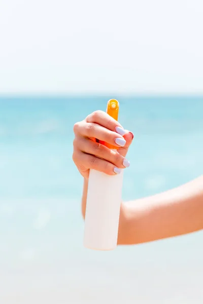 Croped image of woman's hand holding sunscreen spray at the sea background — Stock Photo, Image
