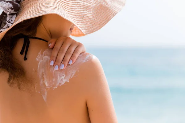 Young girl in straw hat is applying sunscreen on her back to protect her skin — Stock Photo, Image