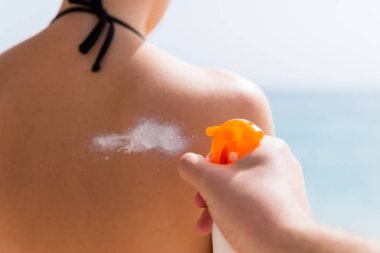 Adamın eli kadının omzuna güneş kremi sürüyor.