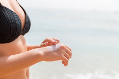 Mayo giymiş bir kadın deniz zeminine parmağıyla güneş kremi sürüyor.