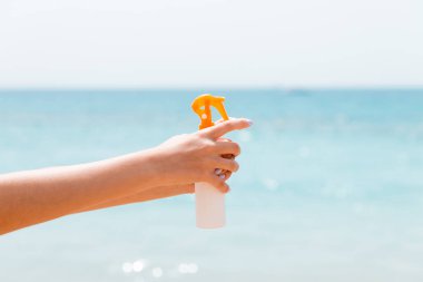 Denizin arka planında elinde güneş kremi tutan bir kadın resmi var.