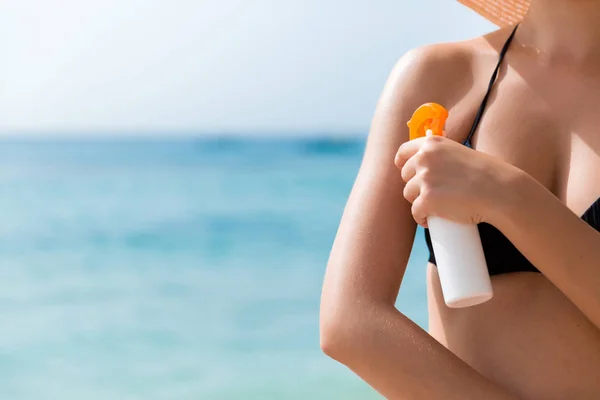Mujer joven está aplicando crema solar protectora en su hombro en la playa — Foto de Stock