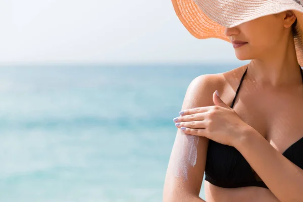 Sonnencreme Sonnencreme. Frau mit Hut trägt Sonnencreme auf der Schulter im Freien bei Sonnenschein an einem schönen Sommertag — Stockfoto