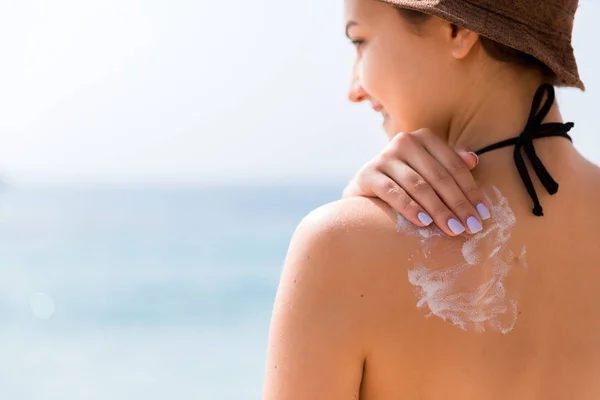 Chica joven con sombrero está aplicando protector solar en su espalda para proteger su piel — Foto de Stock