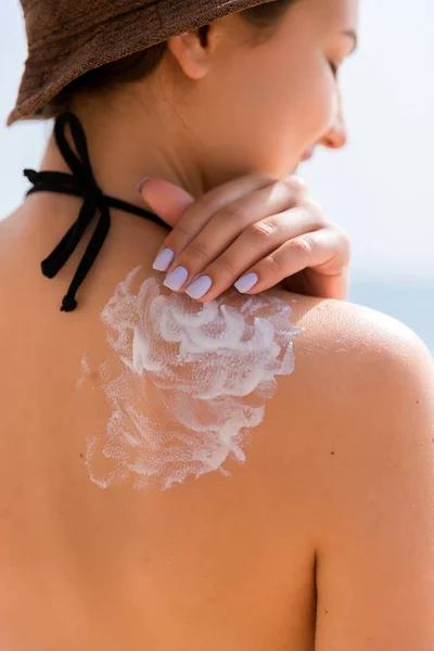 Hermosa mujer con sombrero está poniendo crema solar en su hombro en la playa — Foto de Stock