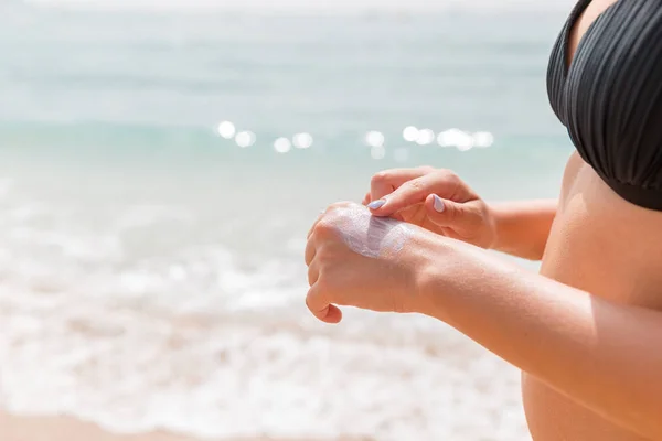 Mujer en traje de baño está aplicando crema solar en su mano con el dedo en el fondo del mar — Foto de Stock