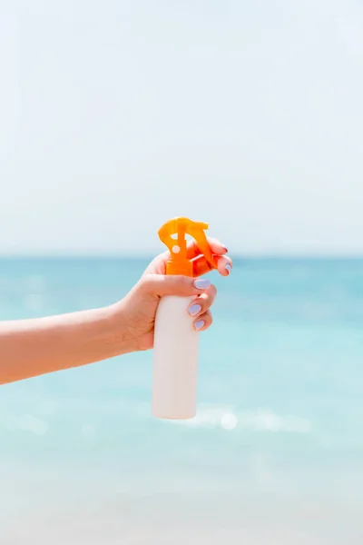 Abgeschnittenes Bild der Hand einer Frau mit Sonnenschutzspray vor dem Hintergrund des Meeres — Stockfoto
