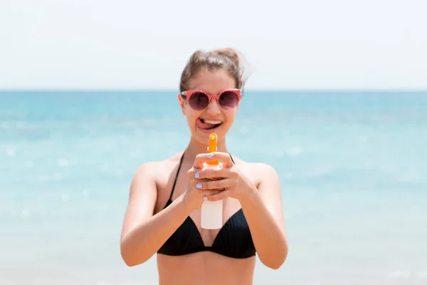 Молодая женщина держит спрей солнцезащитного крема для тела перед камерой на пляже — стоковое фото