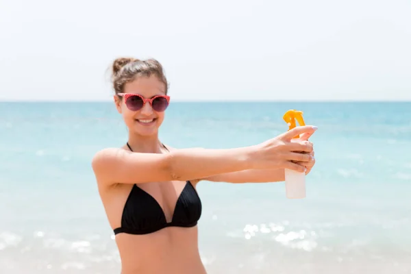 Mujer joven sostiene una botella de protector solar para el cuerpo en el fondo del mar —  Fotos de Stock