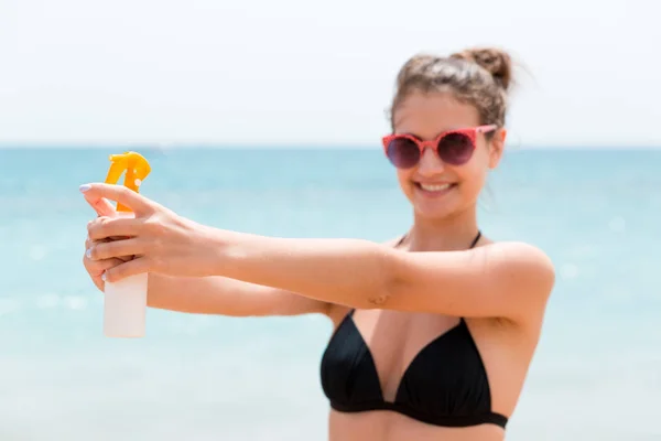 Mujer joven sostiene una botella de protector solar para el cuerpo en el fondo del mar —  Fotos de Stock