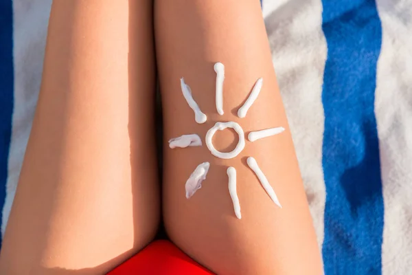 Woman sunbathing on the beach with a drawing of sun on her leg with sunscreen cream