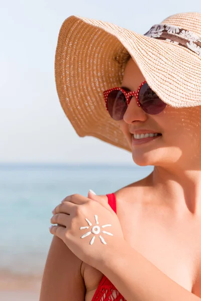 Mujer joven con forma de sol en la mano hecha de protector solar en la playa — Foto de Stock