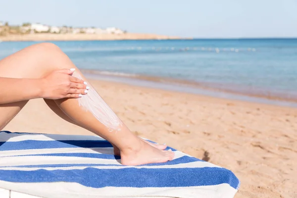 Mujer bonita está aplicando crema solar en su pierna con su mano relajándose en la tumbona junto al mar — Foto de Stock