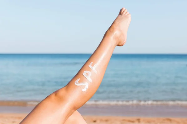 Gamba femminile sollevata con parola sponsale fatta di crema solare in spiaggia. Concetto di fattore di protezione solare — Foto Stock