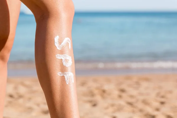 Patas femeninas con palabra spf hechas de crema solar en la playa. Concepto de factor de protección solar — Foto de Stock