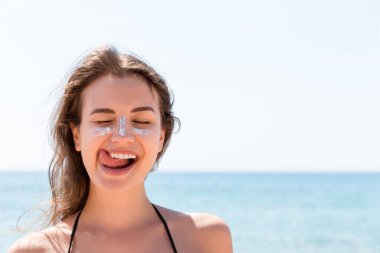 Bronzlaşmış kadın sahilde güneş yanıklarından yüzünü güneş kremiyle koruyor.