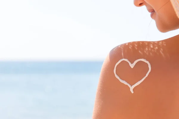 Herz aus Sonnencreme wird am Strand auf die Schulter der Frau gezeichnet — Stockfoto