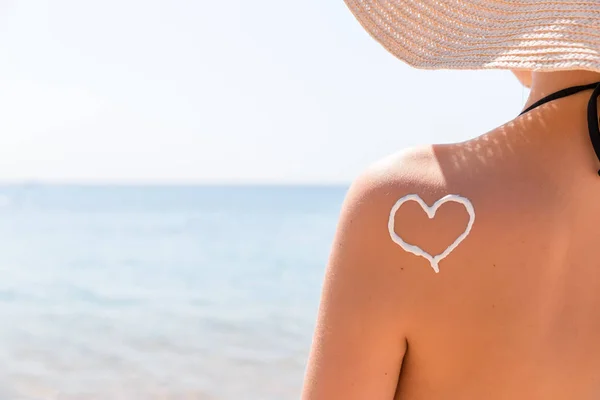 Corazón hecho de crema solar se dibuja en el hombro de la mujer en la playa — Foto de Stock