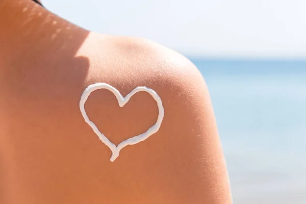 Herz aus Sonnencreme wird am Strand auf die Schulter der Frau gezeichnet — Stockfoto