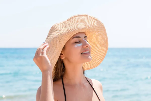 Pretty woman protects her skin on face with sunblock at the beach