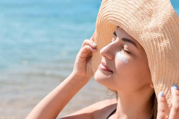 Hübsche Frau schützt ihre Gesichtshaut mit Sonnencreme am Strand — Stockfoto