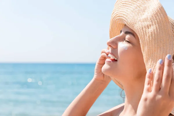 Una mujer sonriente con sombrero se pone protector solar en la cara. Estilo indio — Foto de Stock