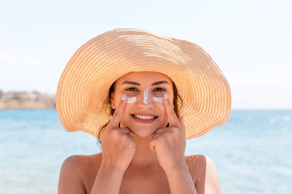 Smiling woman in hat is applying sunscreen on her face. Indian style — Stock Photo, Image