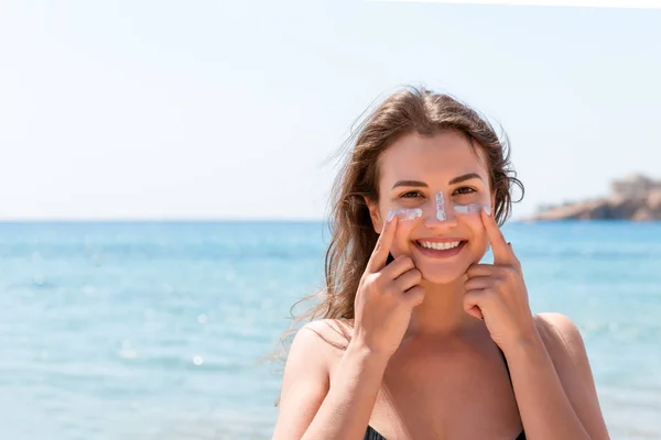 Tanned woman protects her face with sun cream from sunburn at the beach — Stock Photo, Image