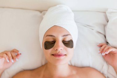 Yatakta yatan bornoz göz yamaları altında ile güzel genç kadın. Mutlu kız kendi başının çaresine bakıyor. Güzellik cilt bakımı ve sağlıklı yaşam sabah konsepti