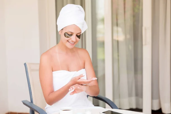 Feliz chica sonriente unta las manos con crema hidratante de la piel. Joven hembra aplicando crema corporal. Belleza cuidado de la piel y bienestar concepto de la mañana — Foto de Stock