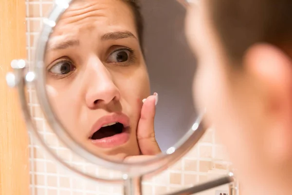 Young girl in front of a bathroom mirror putting cream on a red pimple. Beauty skincare and wellness morning concept