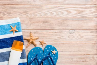 Beach düz döşeme aksesuarları üst görünümü. deniz kabukları, denizyıldızı, havlu ve kopya alanı ile ahşap tahta arka plan üzerinde flip-flop ile güneş kremi şişe