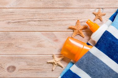 Bir şişe güneş kremi, çizgili mavi havlu ve ahşap arka planda deniz kabukları. Yaz seyahat konsepti. Kopyalama alanı ile üstte görünüm