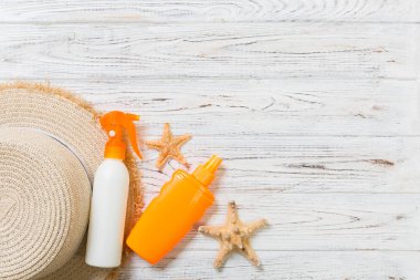 Kopya alanı ile beyaz ahşap masa üzerinde denizyıldızı ve güneş şapkası ile güneş kremi şişeleri. Seyahat sağlık aksesuarları üst görünüm