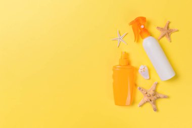 sarı arka plan üzerinde şişelerde denizyıldızı ve deniz kabukları ile güneş kremi, üst görünümü