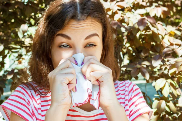 Ung flicka med allergi i höst park. Nysa flicka blåser näsan i en servett — Stockfoto
