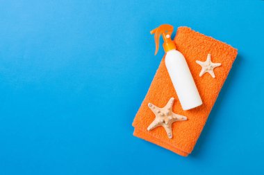 Summer beach flat lay accessories. Sunscreen bottle cream, towel and seashells on colored Background. Travel holiday concept with copy space